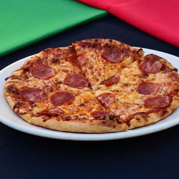 Sliced pepperoni pizza on a white plate, with green and red fabric in the background.