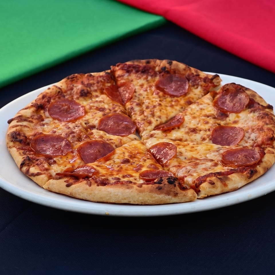 Sliced pepperoni pizza on a white plate, with green and red fabric in the background.