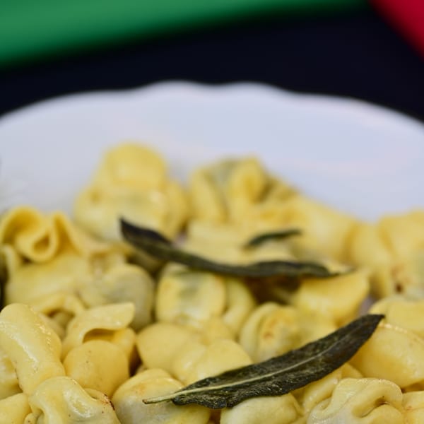 Plate of golden tortellini pasta topped with dark green sage leaves.