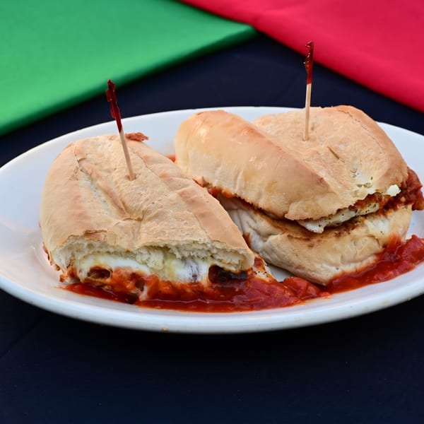 Two cheesy subs with red sauce on a white plate, against green and red fabric.