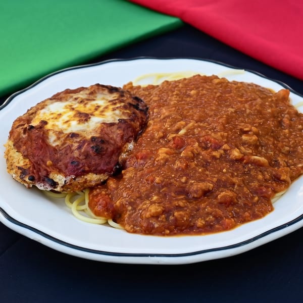Spaghetti with rich meat sauce and a large baked cheesy item on a white plate.
